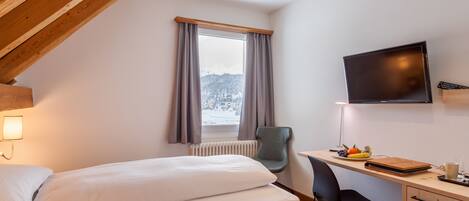 Un dormitorio con cama, escritorio, silla, televisor y ventana con cortinas.