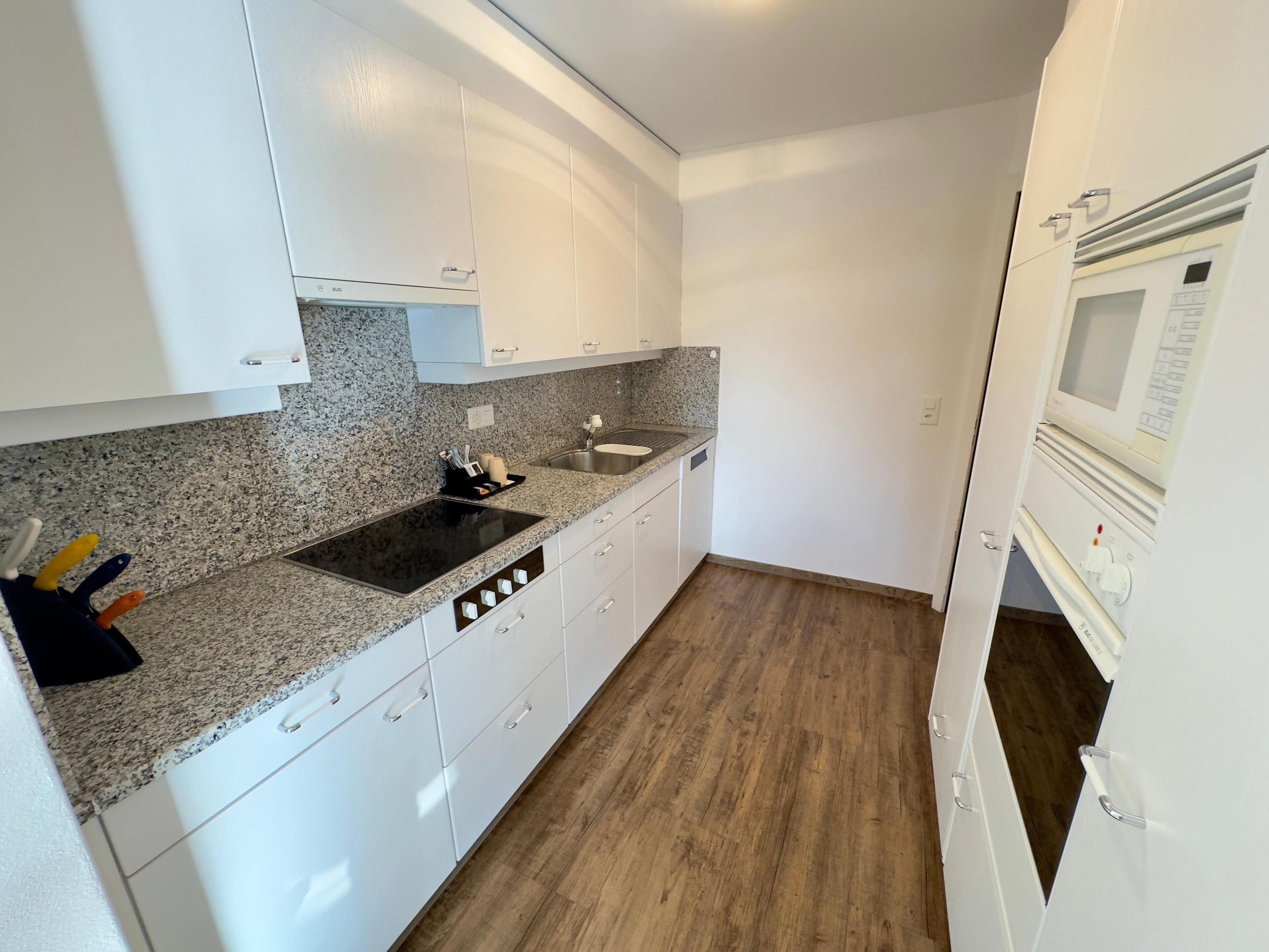 A compact kitchen with white cabinets, a granite countertop, a sink, and a built-in oven.