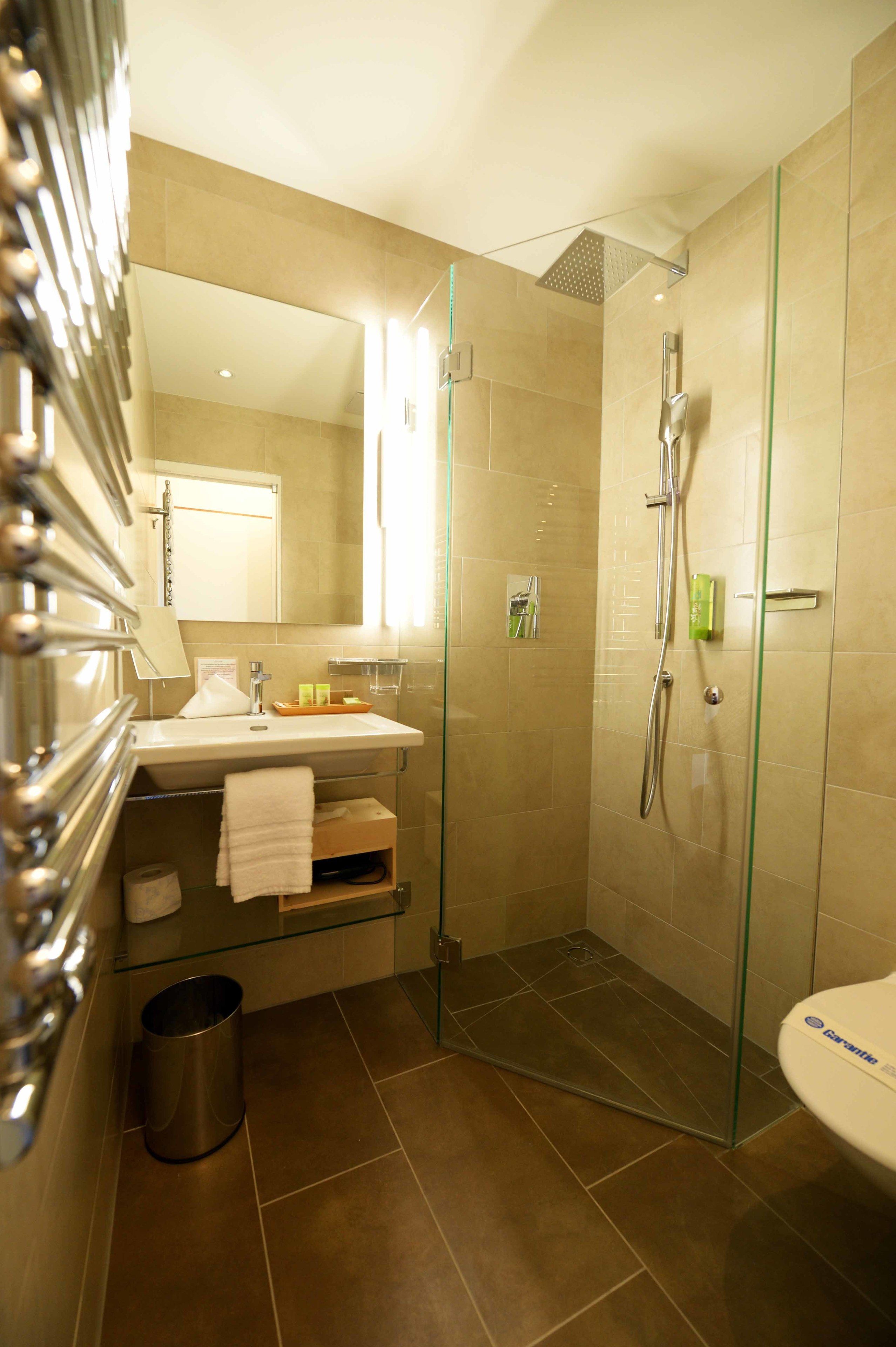A modern bathroom with a glass-enclosed shower, a sink with a mirror, and a trash bin.