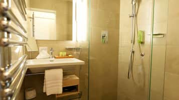 Un baño moderno con ducha de vidrio, lavamanos con espejo y un cesto de basura.
