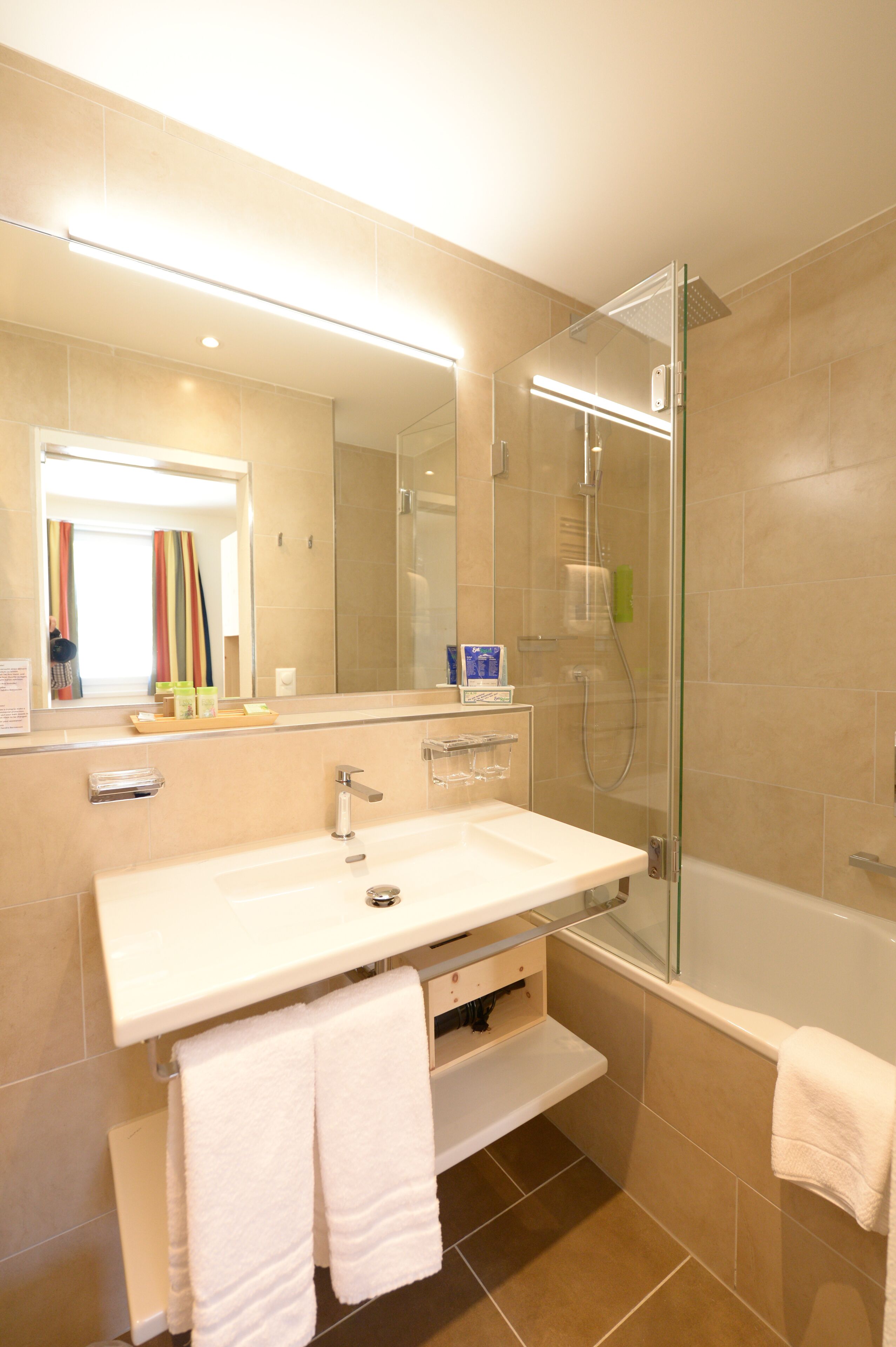 Une salle de bain moderne avec une douche à parois de verre, un grand miroir et un lavabo blanc.