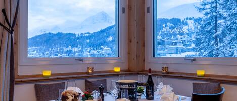 Ein Esstisch für zwei Personen mit Blick auf schneebedeckte Berge und eine Stadt.