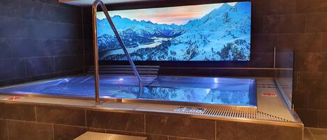 Un jacuzzi con vista a la montaña, paredes de azulejos y una escalera de metal.