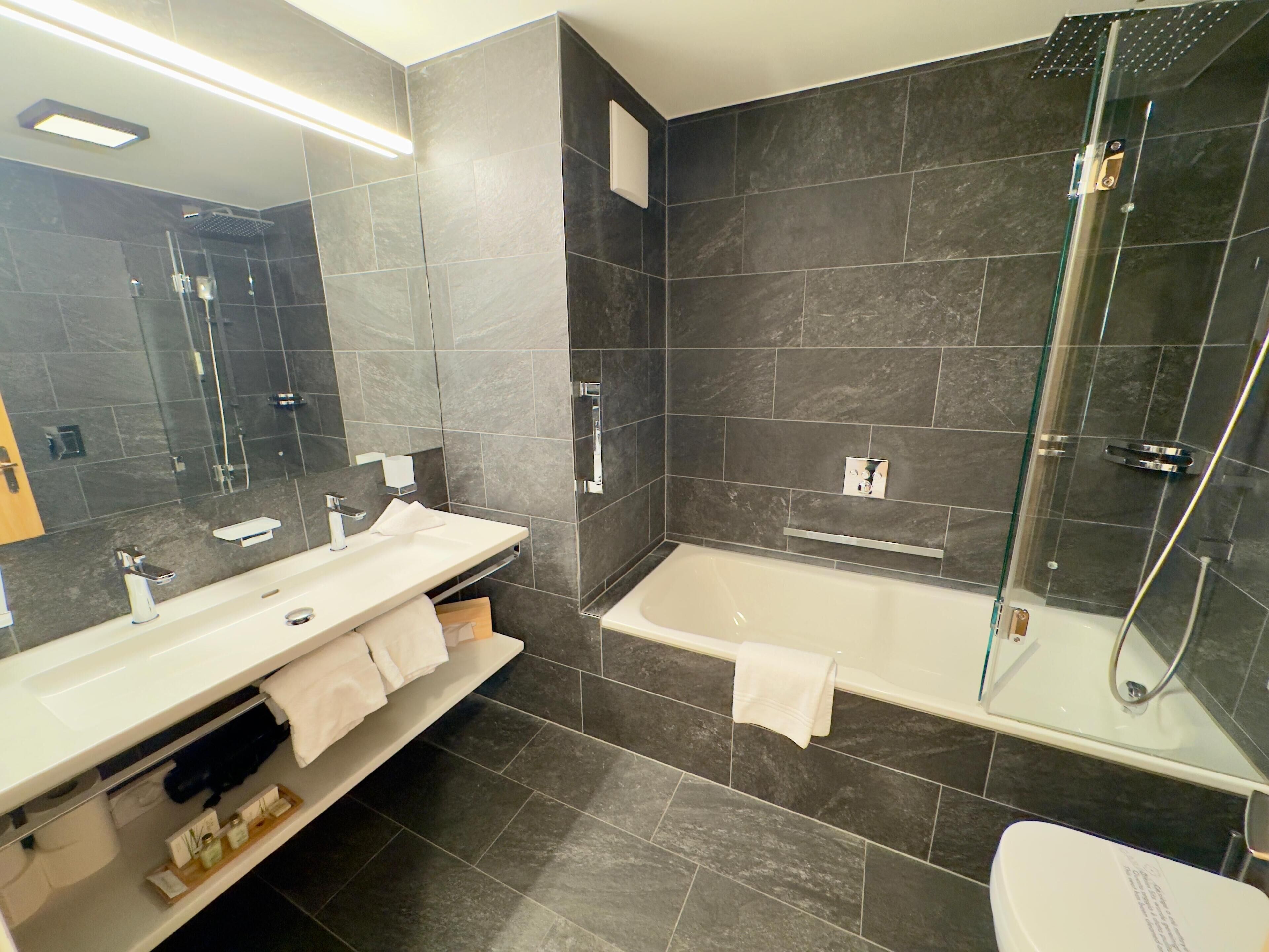 A modern bathroom with a large mirror, a white sink, a bathtub, and a glass-enclosed shower.