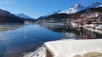 A lakeside view with snow-covered mountains and a town in the background.