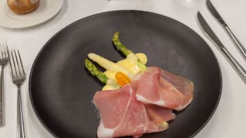 A black plate with asparagus and prosciutto on a white tablecloth.