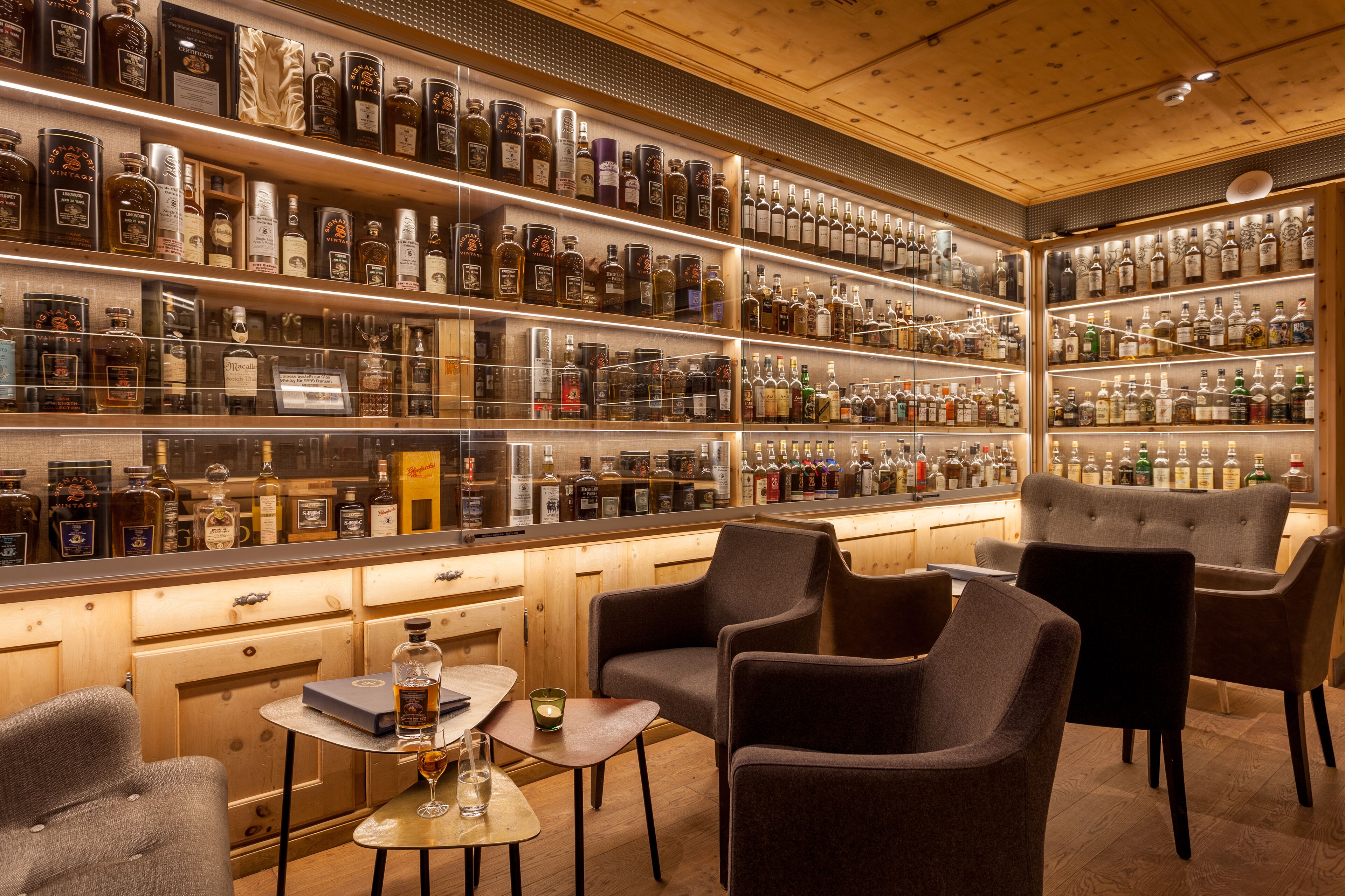 A bar area with shelves of liquor bottles, a bar counter, and seating.