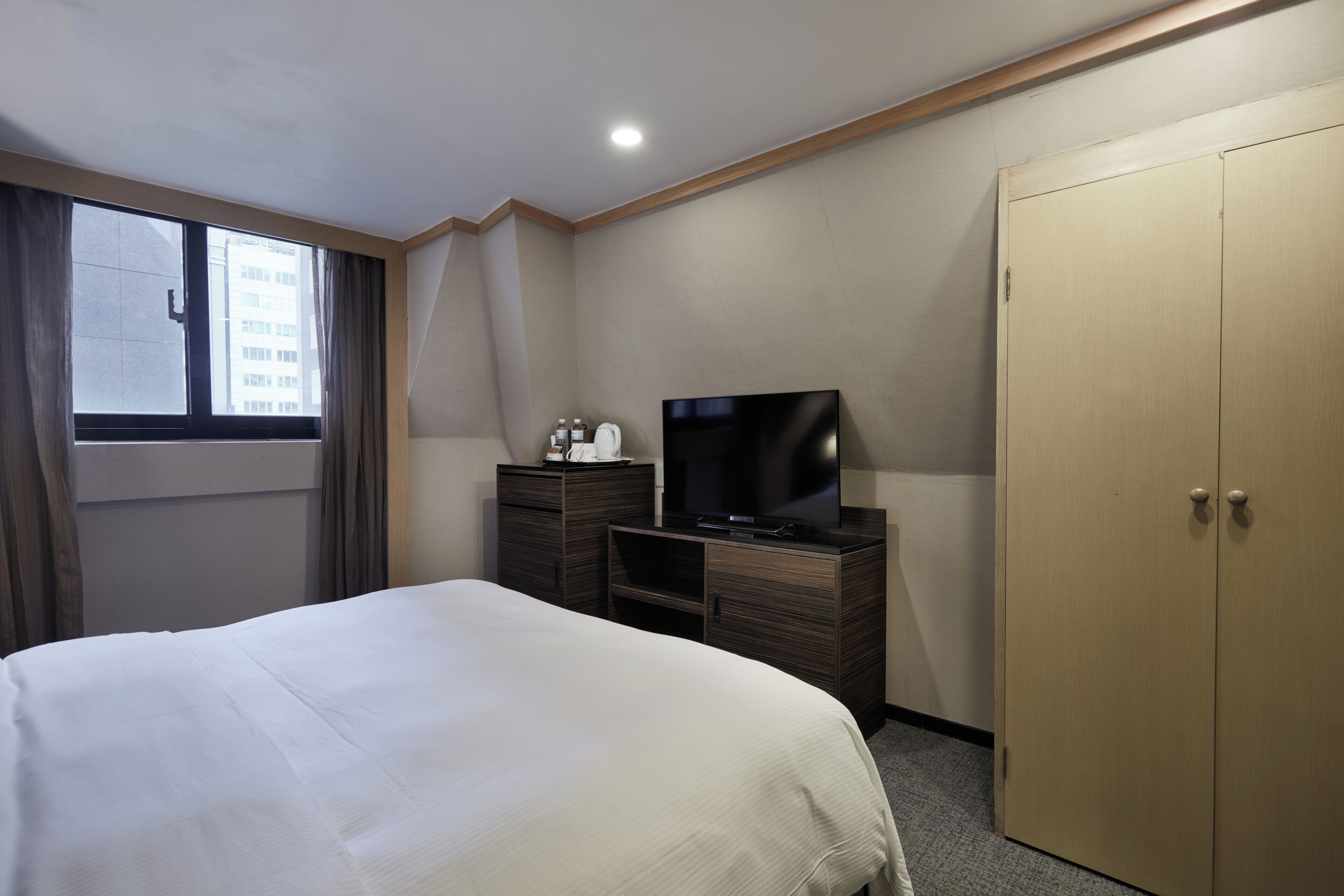Une chambre d’hôtel équipée d’un lit, d’une télévision, d’une commode, d’une armoire et d’une fenêtre avec des rideaux.