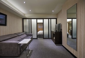 Een moderne hotelkamer met een bank, een flatscreen televisie, een grote spiegel en een schuifdeur naar een slaapkamer.