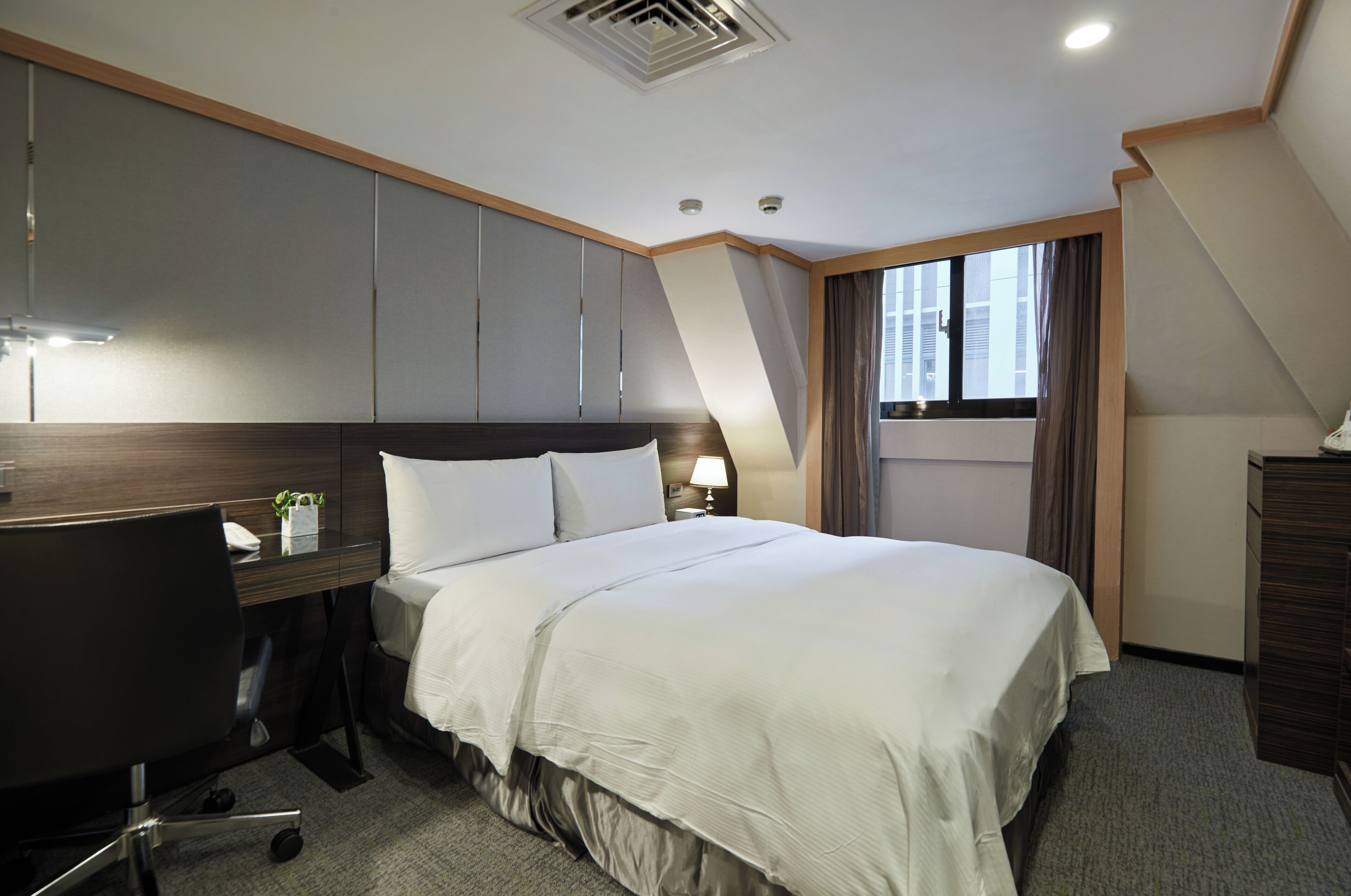 A hotel room with a bed, desk, and a window with curtains.