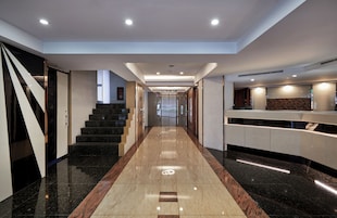 Een moderne hotel lobby met een marmeren vloer, een trap en een receptiebalie.