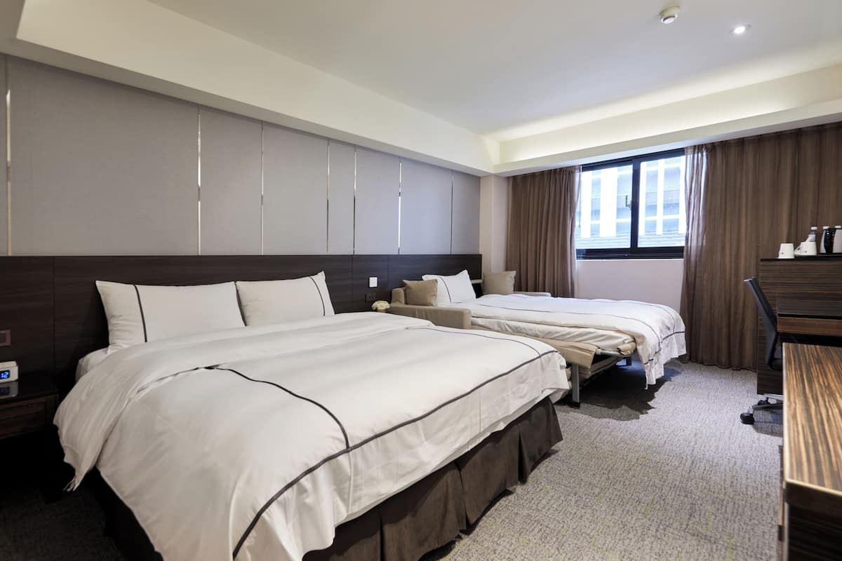 A hotel room with two beds, a desk, a wardrobe, and a window with curtains.