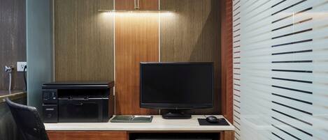 A hotel room with a wooden desk, a flat-screen TV, a printer, and a chair.