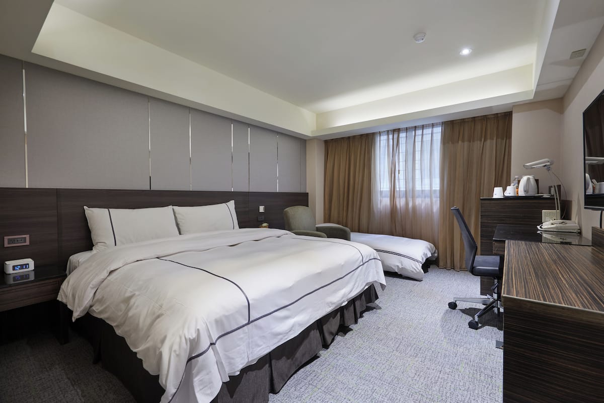A hotel room with a large bed, a desk, a chair, and a wardrobe.