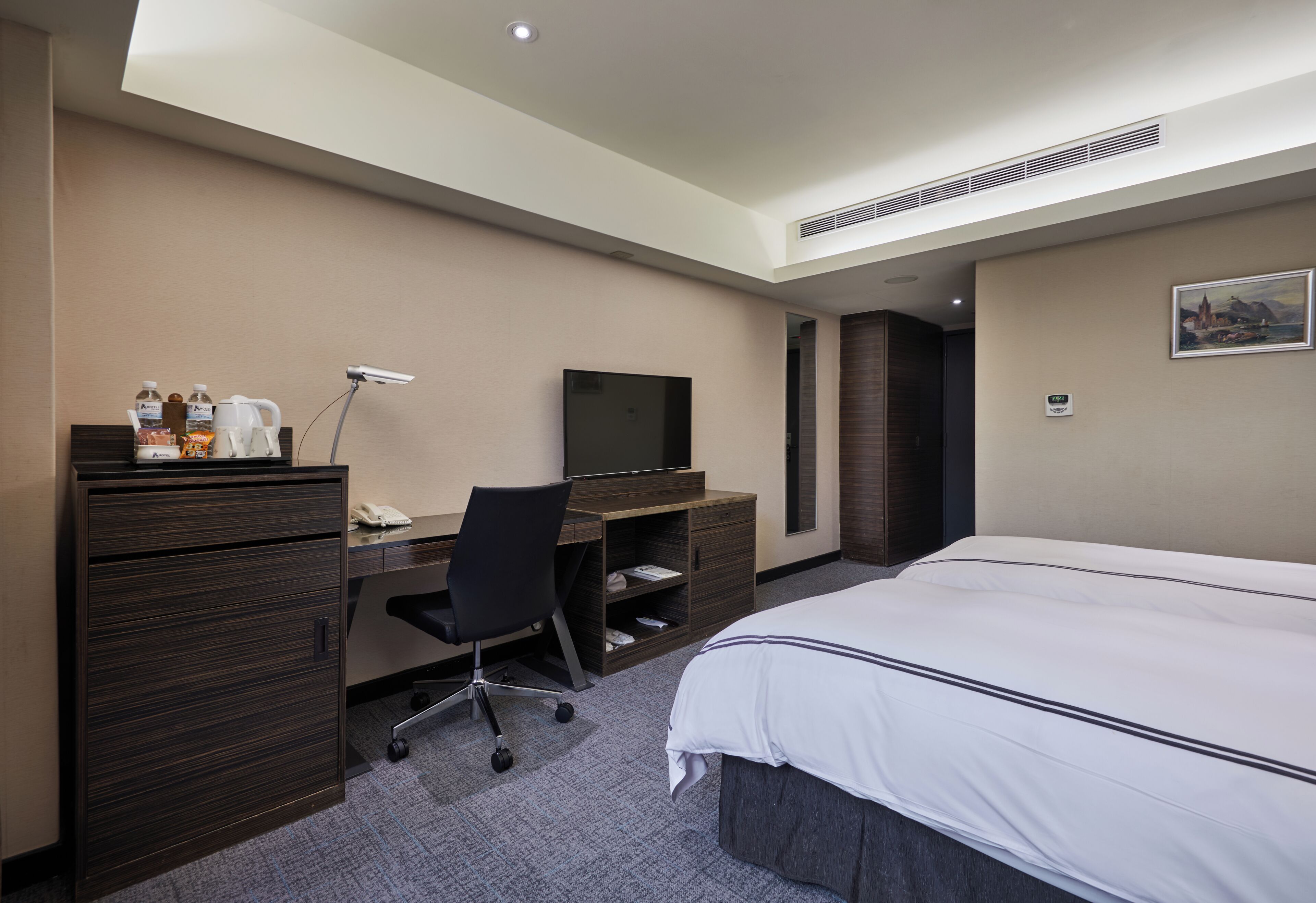 Una camera d'albergo con un letto, una scrivania con una sedia, una televisione, un minibar e un quadro appeso al muro.