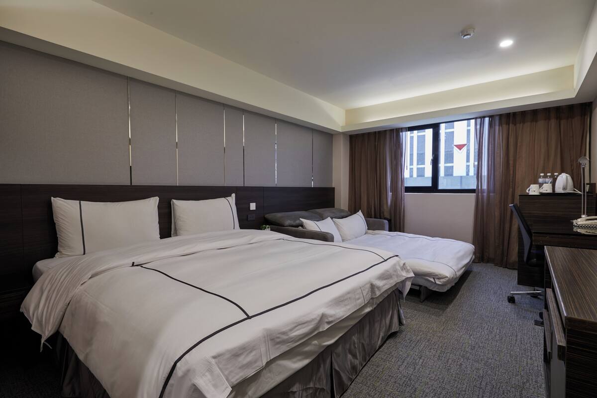 A hotel room with two beds, a desk, a chair, a wardrobe, and a window with curtains.