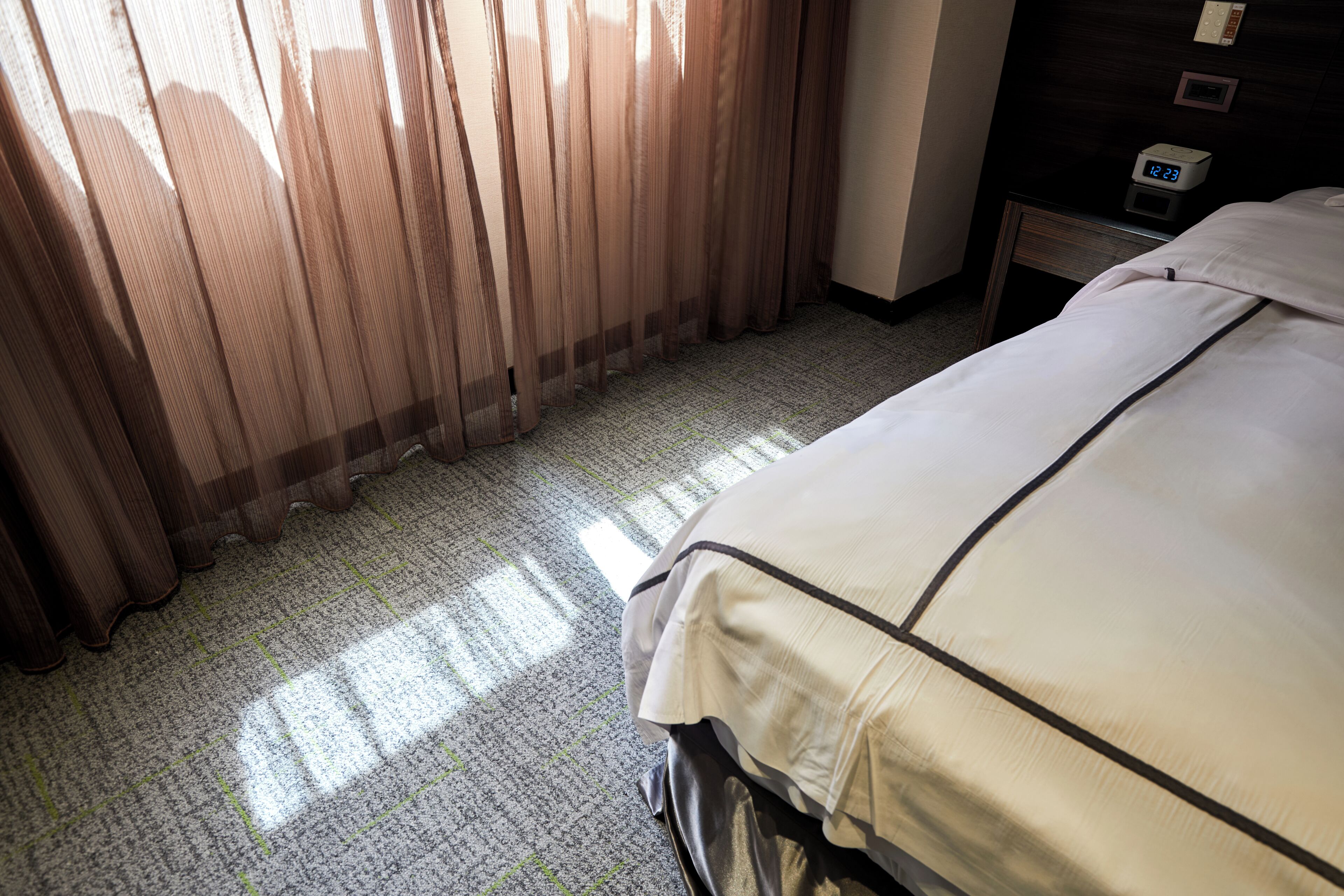 A hotel room with a bed, curtains, a nightstand, and a clock.