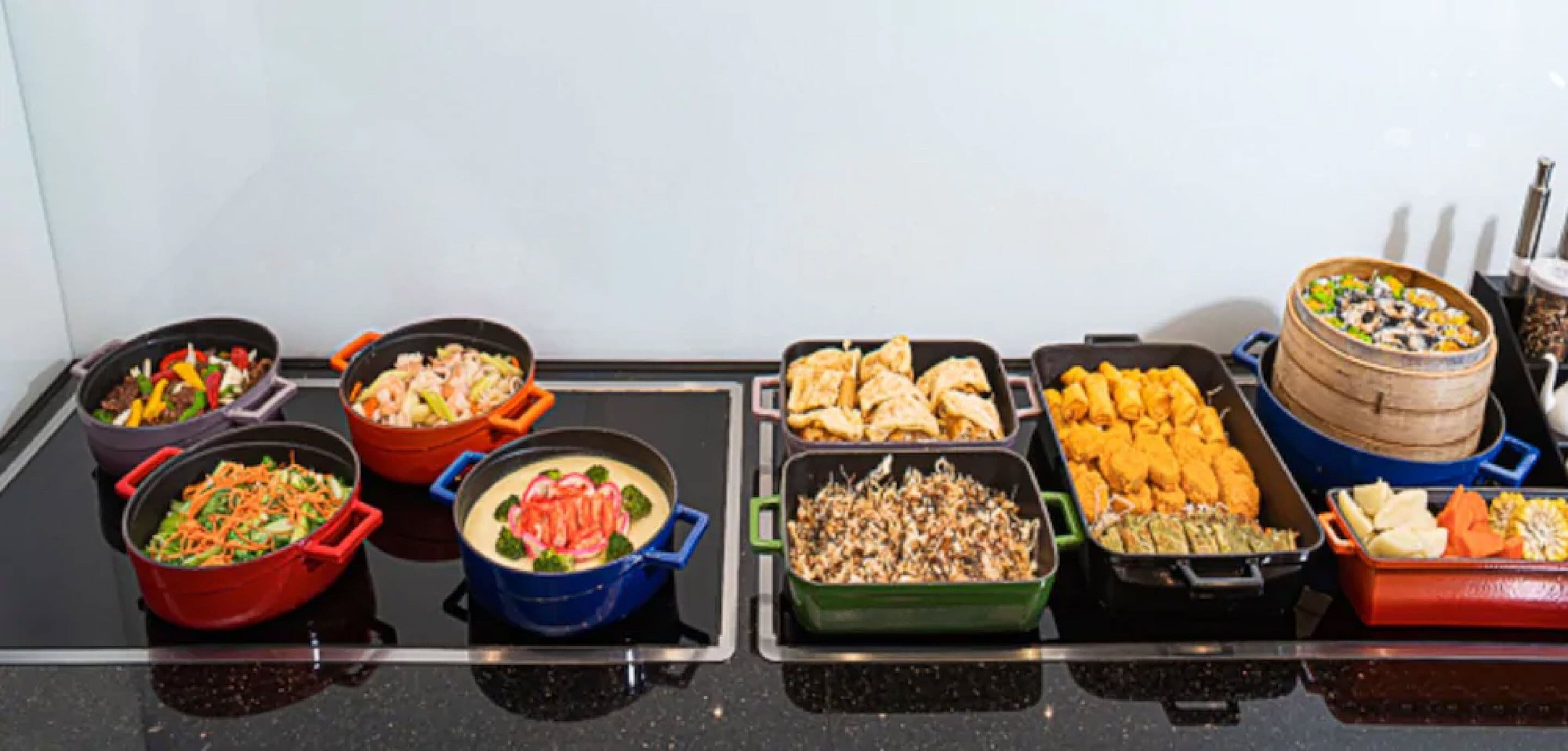 A buffet table with various dishes in different colored serving containers.