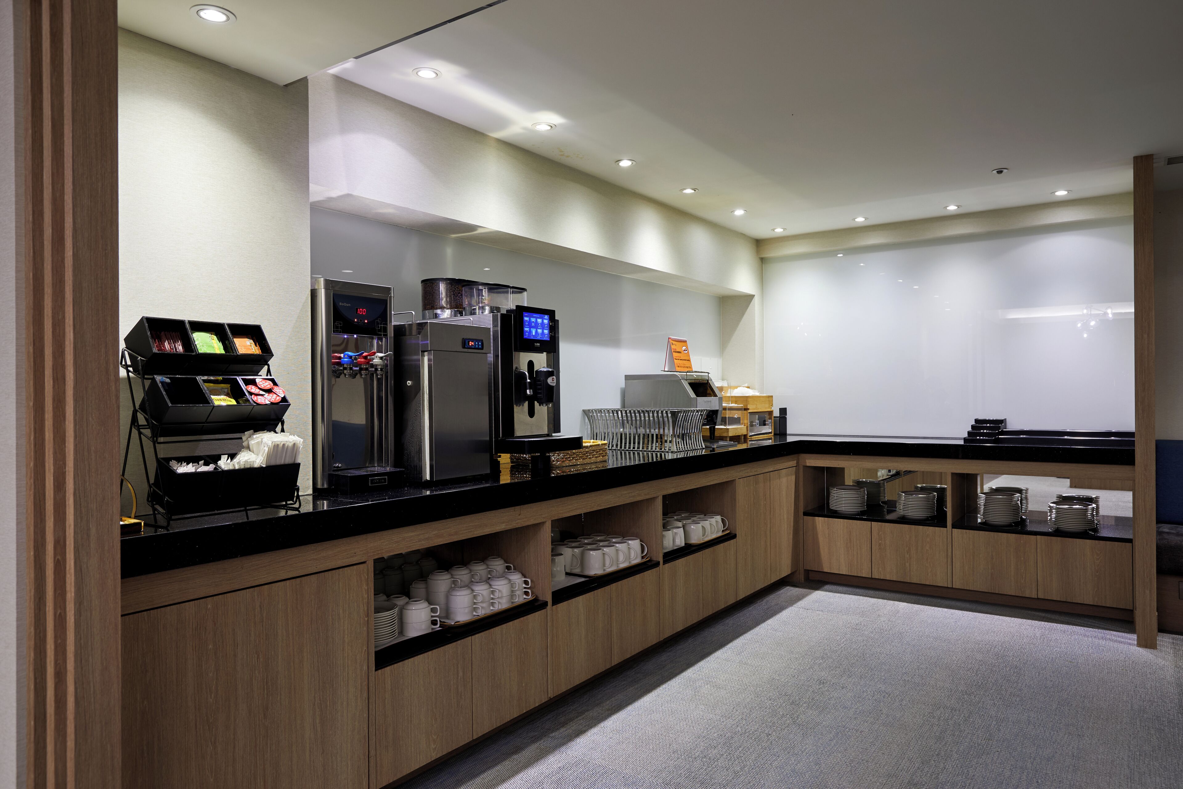 A modern hotel kitchen with a coffee machine, refrigerator, and buffet area.