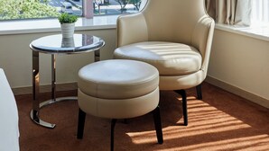 A hotel room with a large window, a beige armchair, a matching ottoman, and a small round table with a plant. - K Hotel - Taipei II (Taipei)