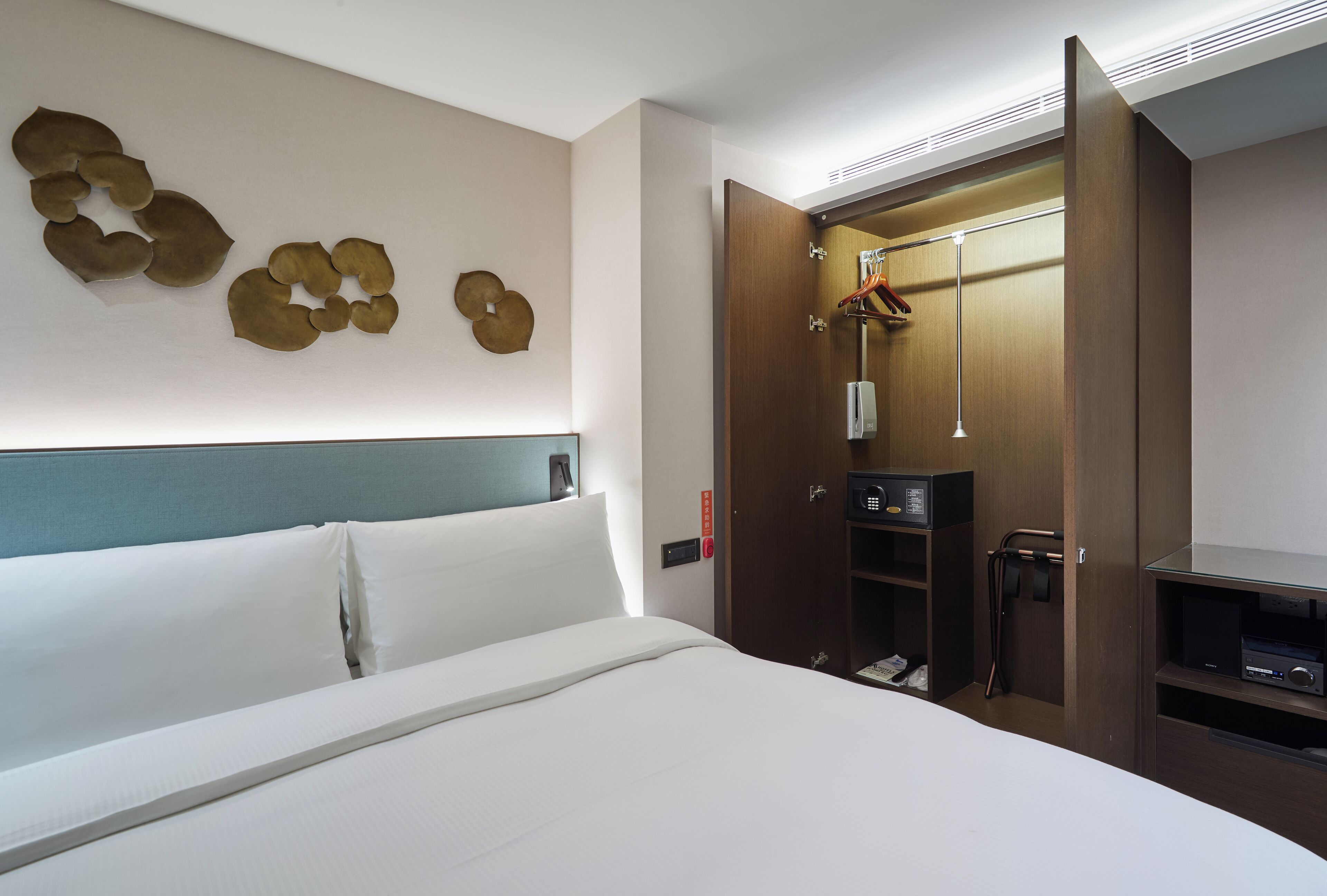 A hotel room with a bed, a wardrobe, and a wall-mounted artwork.