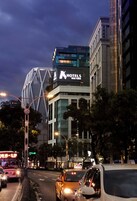 Un hotel moderno con un llamativo letrero que dice 'HOTELES', rodeado de tráfico urbano y edificios.