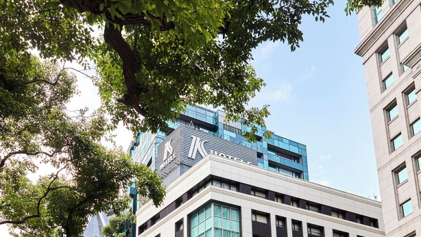 A modern building with a prominent glass facade, a corner entrance, and a street view with a clear sky. - K Hotel - Taipei II (Taipei)