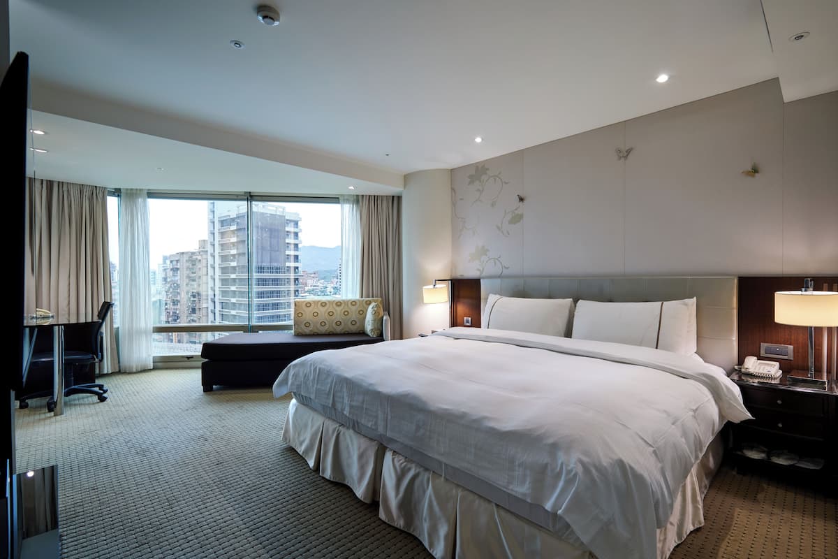Habitación de hotel con una cama grande, un escritorio, una silla, una ventana con cortinas y vistas a edificios.