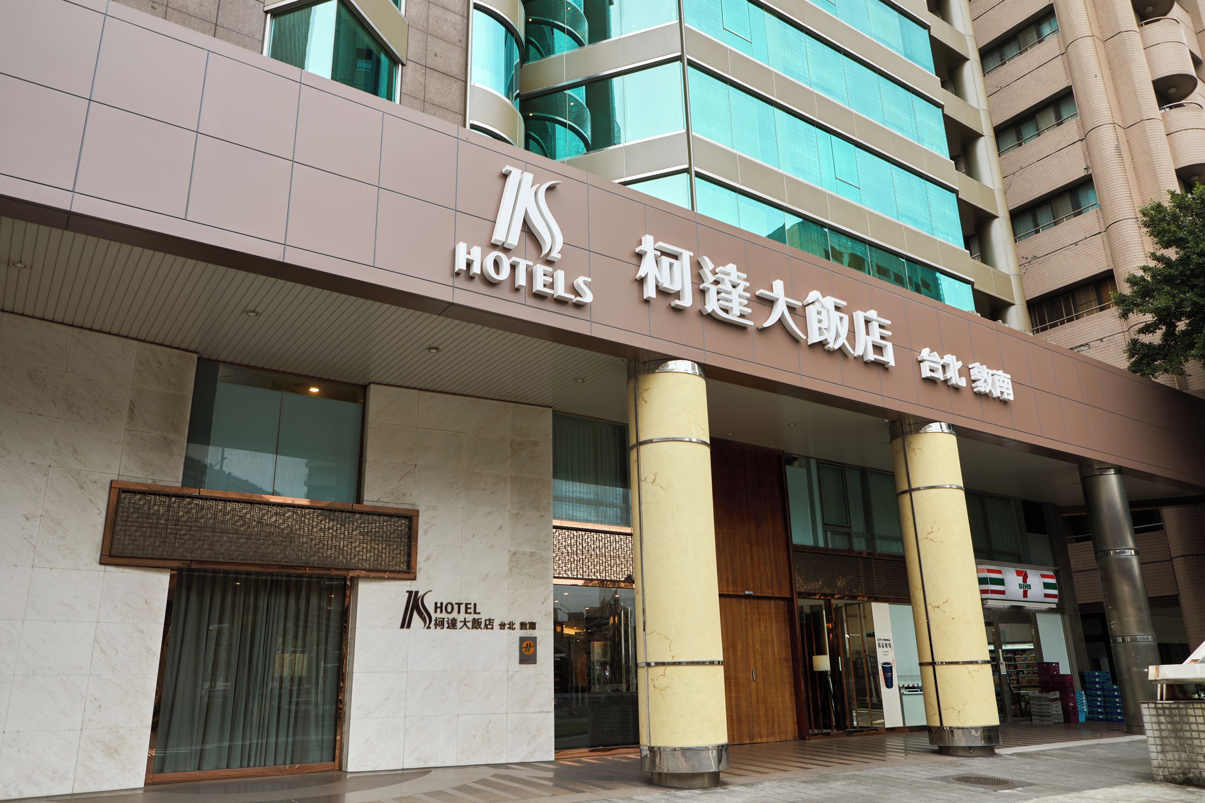 A hotel entrance with a sign in multiple languages, large pillars, and a modern facade.