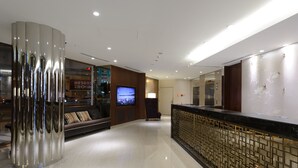 Un vestíbulo moderno con una mesa de recepción, un televisor de pantalla grande, un sofá con cojines y un panel decorativo en la pared.