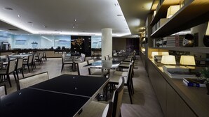 Un restaurante moderno con varias mesas y sillas, un área de cocina y una estantería con libros y objetos decorativos.