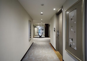 A hallway with a patterned carpet, framed artwork on the walls, and a door with a decorative panel. - K Hotels Dunnan (Taipei)
