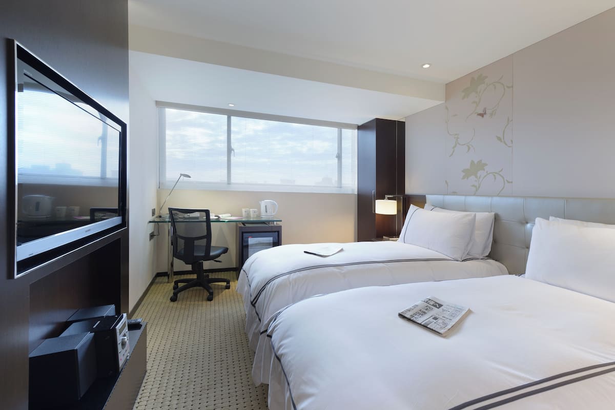 Habitación de hotel con dos camas, un escritorio con computadora, una silla y un televisor.