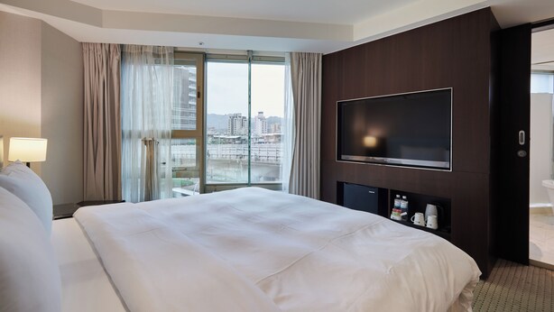 Habitación de hotel con una cama grande, televisión, escritorio con lámpara y vista a la ciudad desde la ventana.