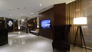 Un vestíbulo moderno con una pantalla de televisión grande, un área de estar cómoda y un ventanal de pared a techo con cortinas.