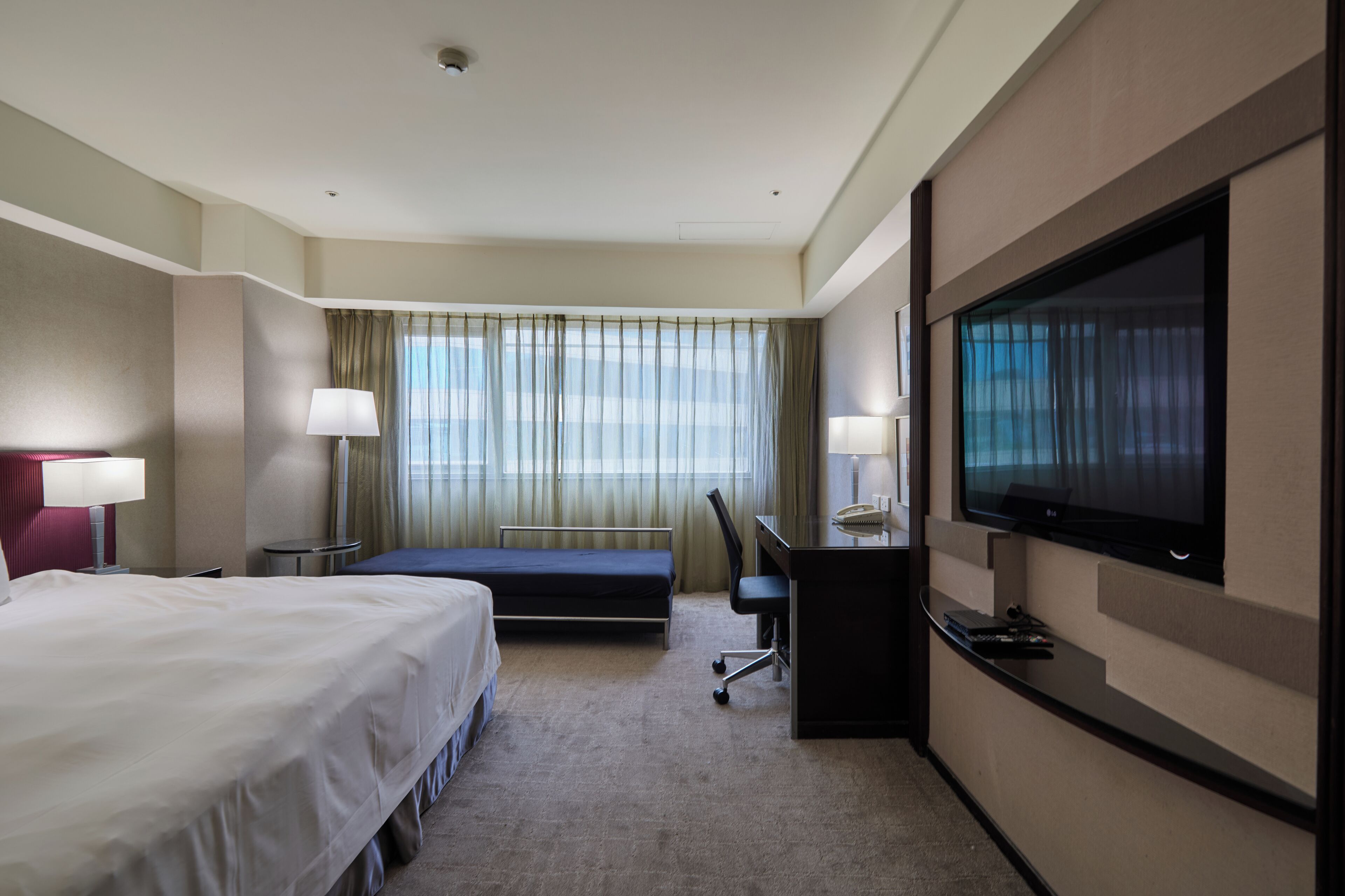 A hotel room with a bed, desk, chair, television, and curtains.
