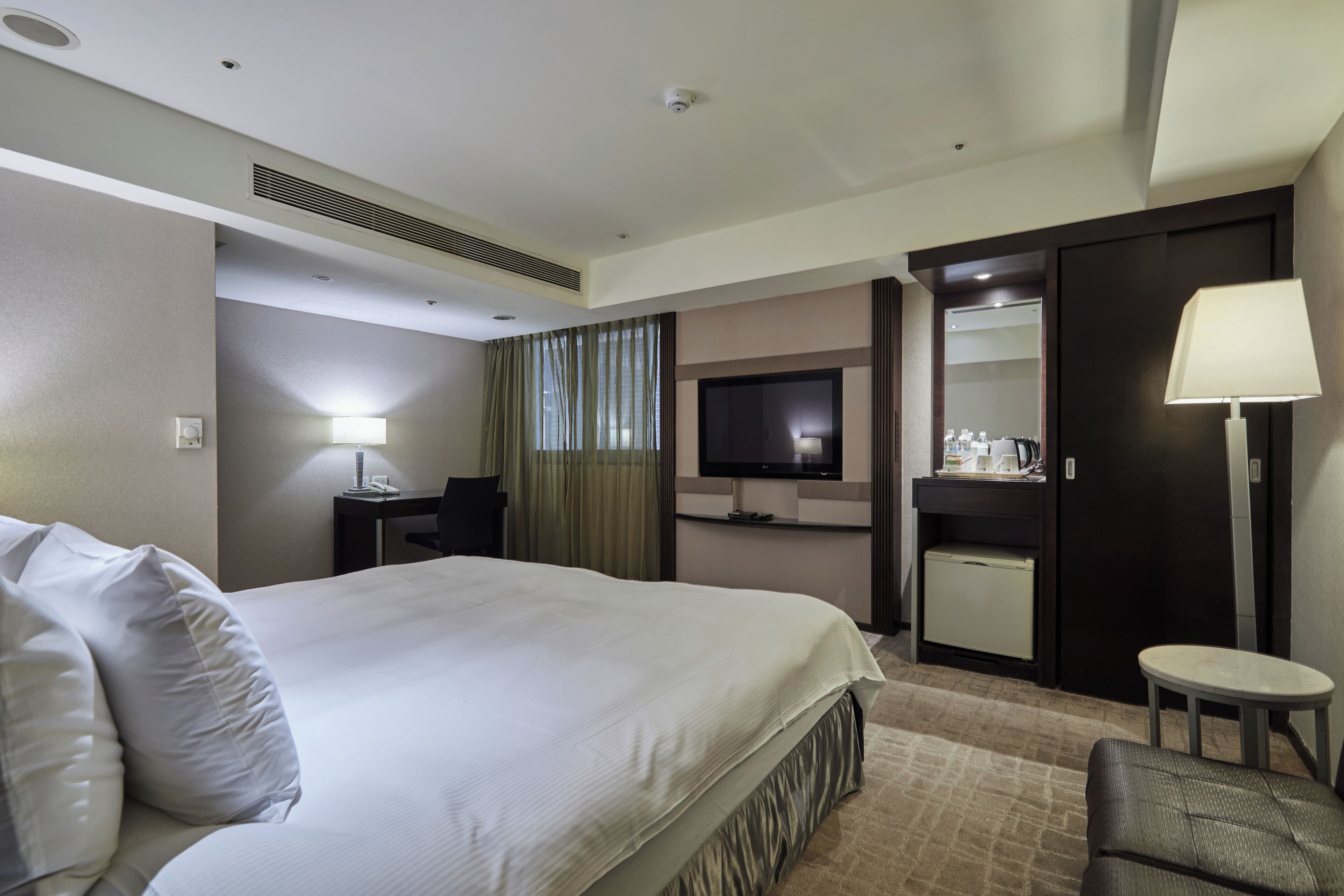 Une chambre d’hôtel équipée d’un lit, d’un bureau, d’une télévision, d’un mini-bar et d’un coin salon.