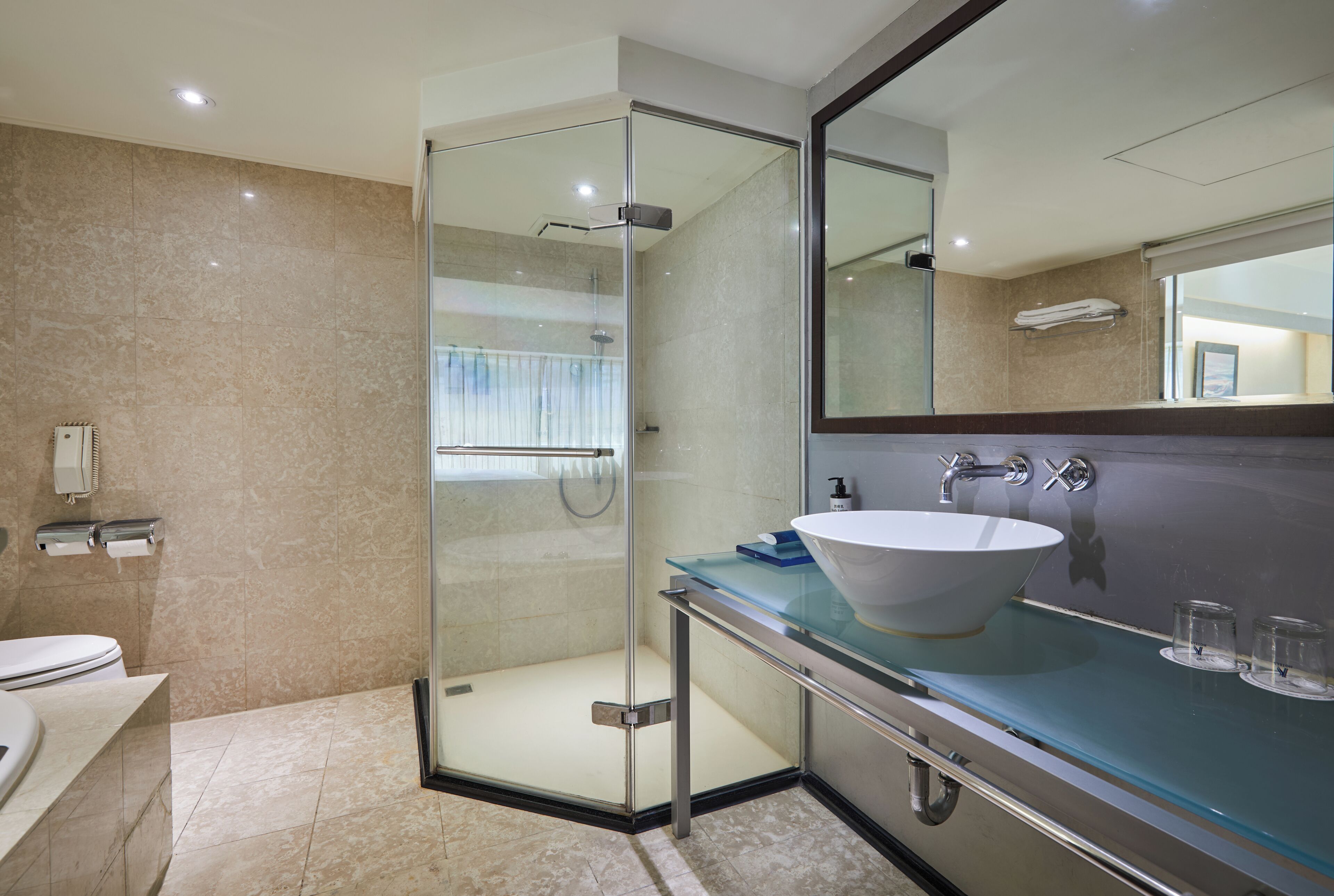 A modern bathroom with a glass-enclosed shower, a large mirror, and a glass countertop with a sink.