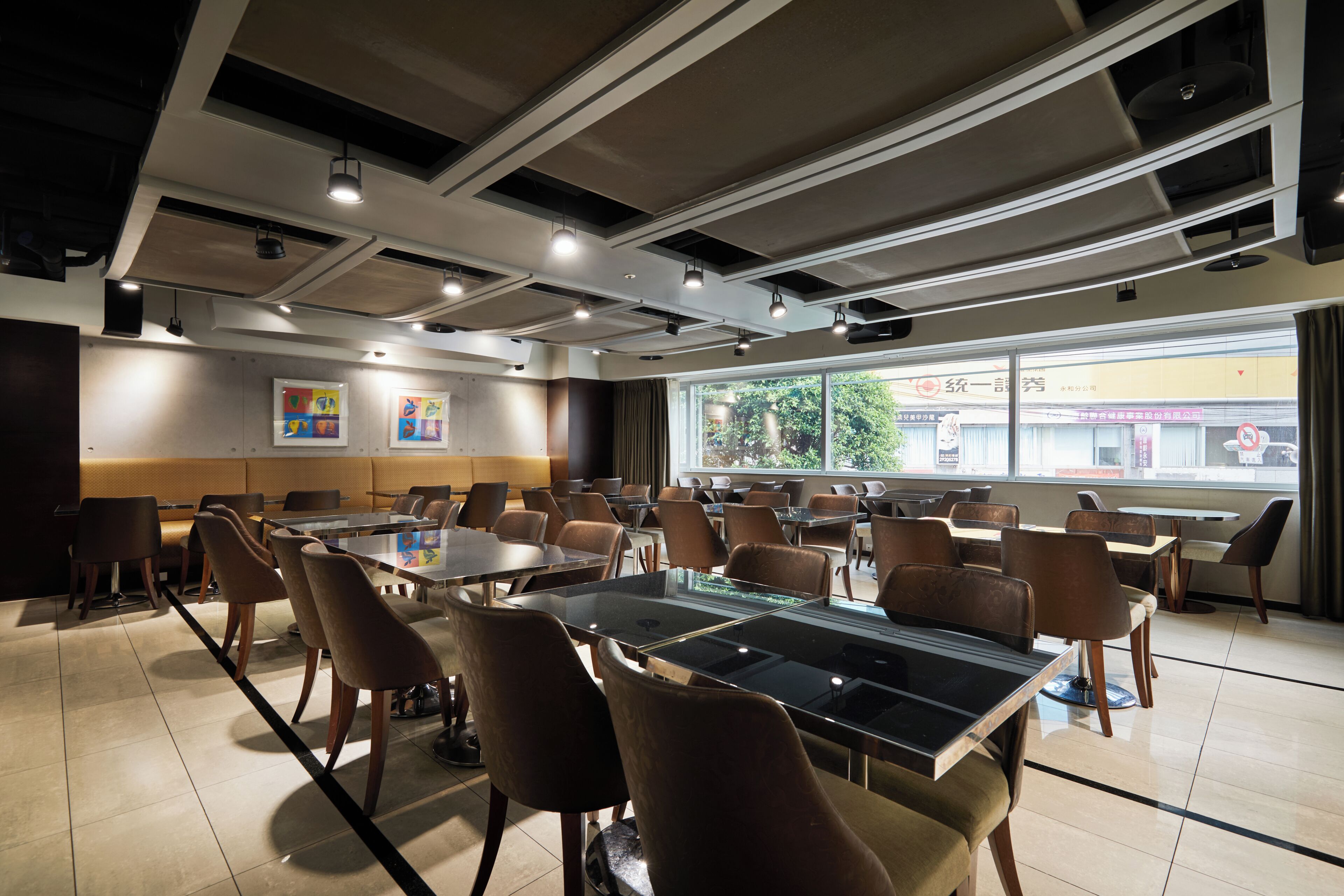 A modern conference room with glass tables and chairs, large windows, and ceiling lights.
