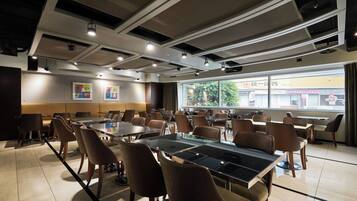 A modern conference room with glass tables and chairs, large windows, and ceiling lights.