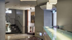 Een moderne lobby met een marmeren vloer, een glazen receptiebalie en een trap.