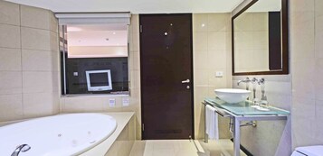 Un baño moderno con una bañera grande, un tocador de vidrio con lavabo blanco y una puerta oscura.