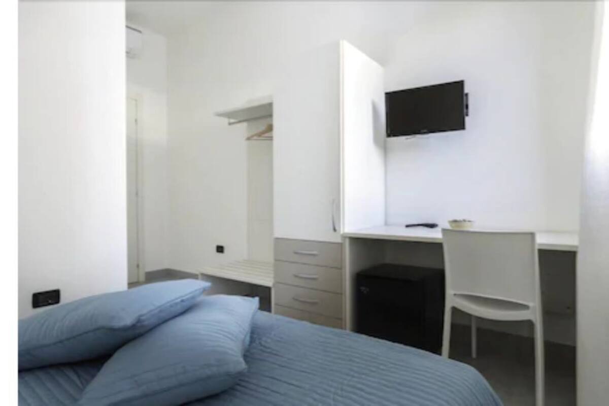 A bedroom with a bed, a desk, a chair, and a TV mounted on the wall.