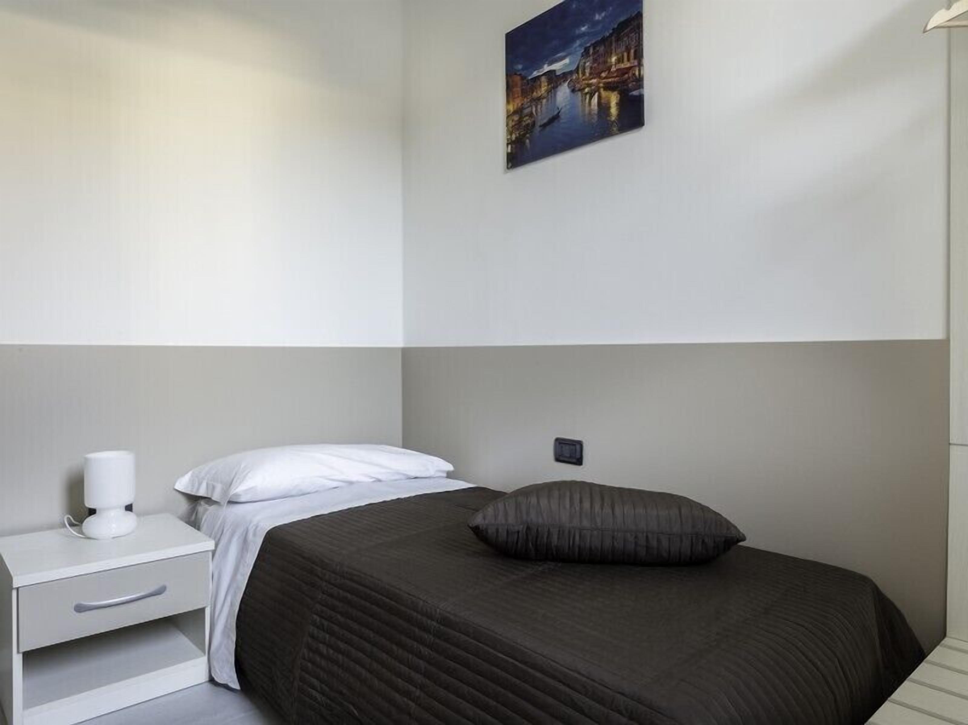 Una camera da letto con un letto, un comodino con una lampada e un quadro appeso al muro.