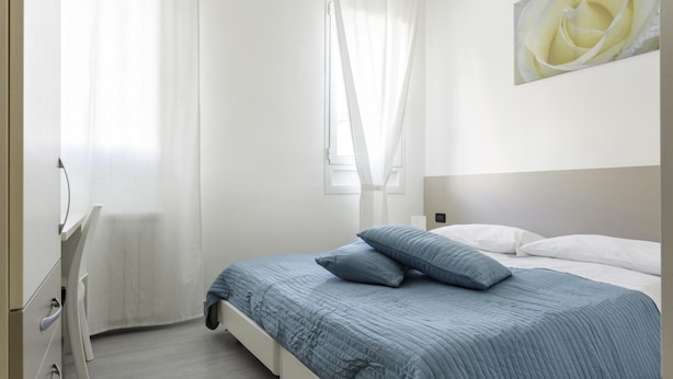 A bedroom with a bed, white curtains, a painting of a rose, and a dresser. - Easy Venice Room (Mestre)