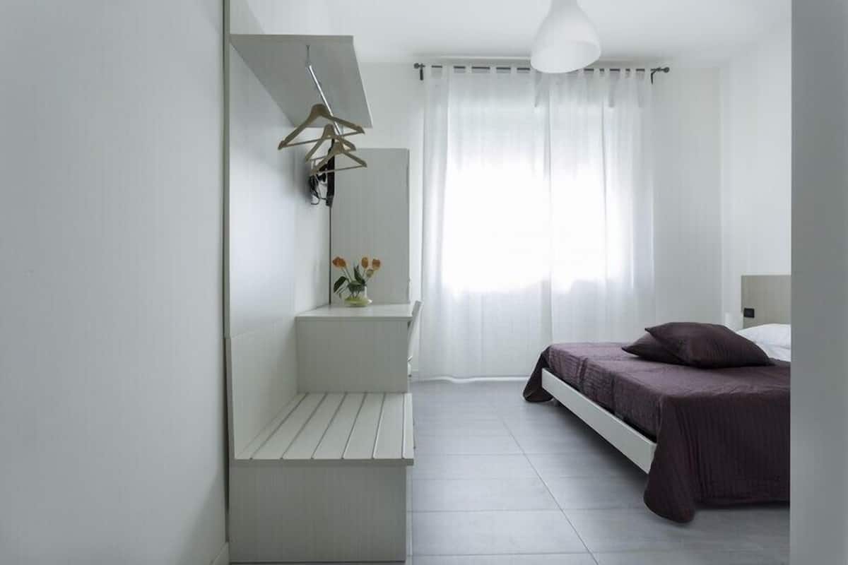 A modern bedroom with a bed, a bench, a hanging light, and a window with curtains.