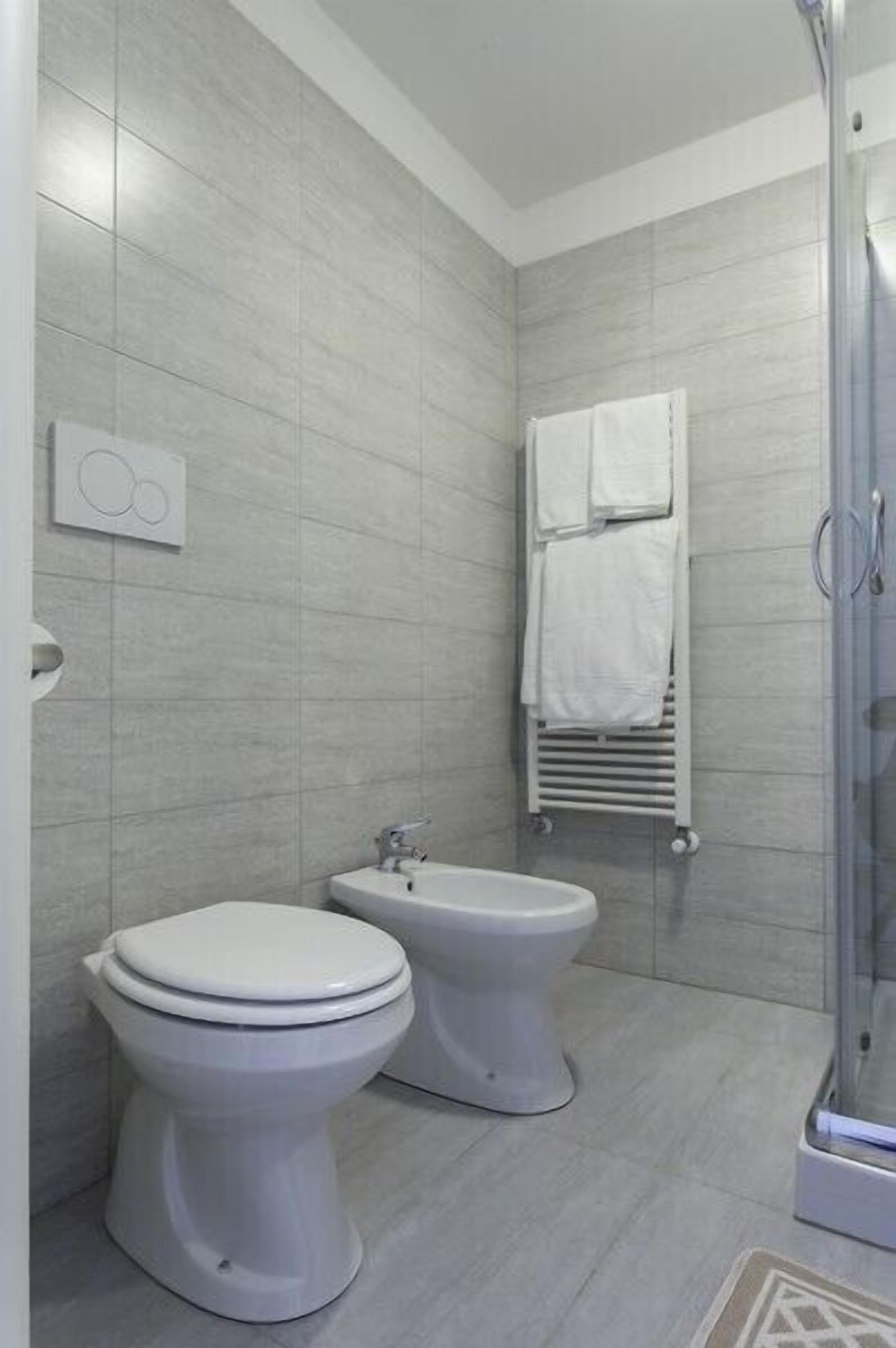 Un bagno moderno dotato di due servizi igienici, una doccia e un porta asciugamani.