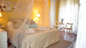 A bedroom with a canopy bed, a bedside table with a lamp, a chair, and a small table with a plant. - At Home Bed and Breakfast (Lucca)
