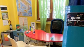 Una habitación pequeña y colorida con una mesa roja, dos sillas blancas, un armario azul y un mapa en la pared.