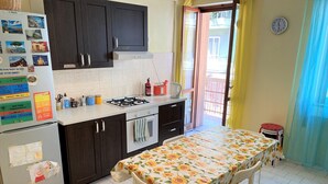 Una cocina compacta con armarios oscuros, una estufa a gas, un refrigerador y una mesa de comedor con mantel de girasoles.